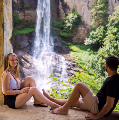 Two travellers sat looking out at a waterfall in Sri Lanka.