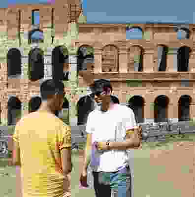 Two male travellers stood talking in front of the Rome Colosseum.