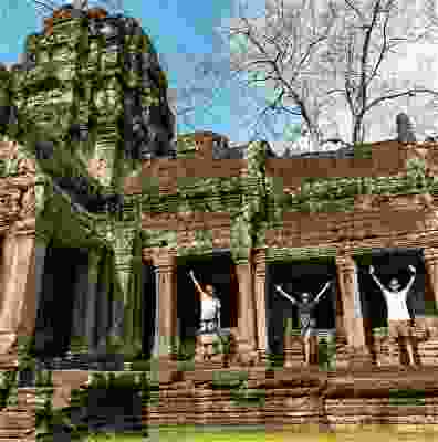 Travellers standing in front of the Bayon temple with their hands in the air.