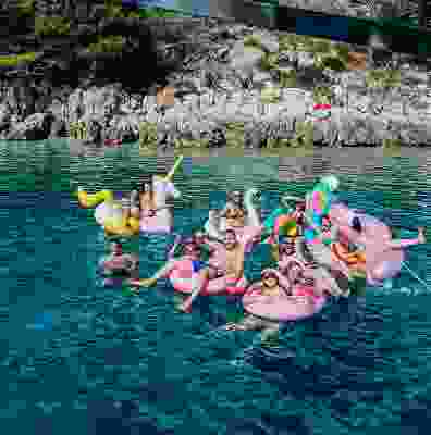 Group of travellers smiling whilst on floats in the sea at a party.