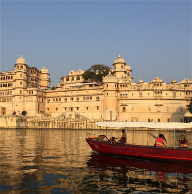 Long boat sailing past traditional buildings in Udaipur.