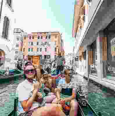 Travellers riding in a gondola down busy Venice..